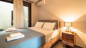 A hotel room with a bed, a bedside lamp, a nightstand, and an air conditioning unit.