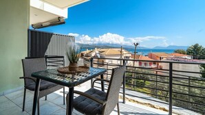 A balcony with a table and chairs, a potted plant, and a view of buildings and mountains.