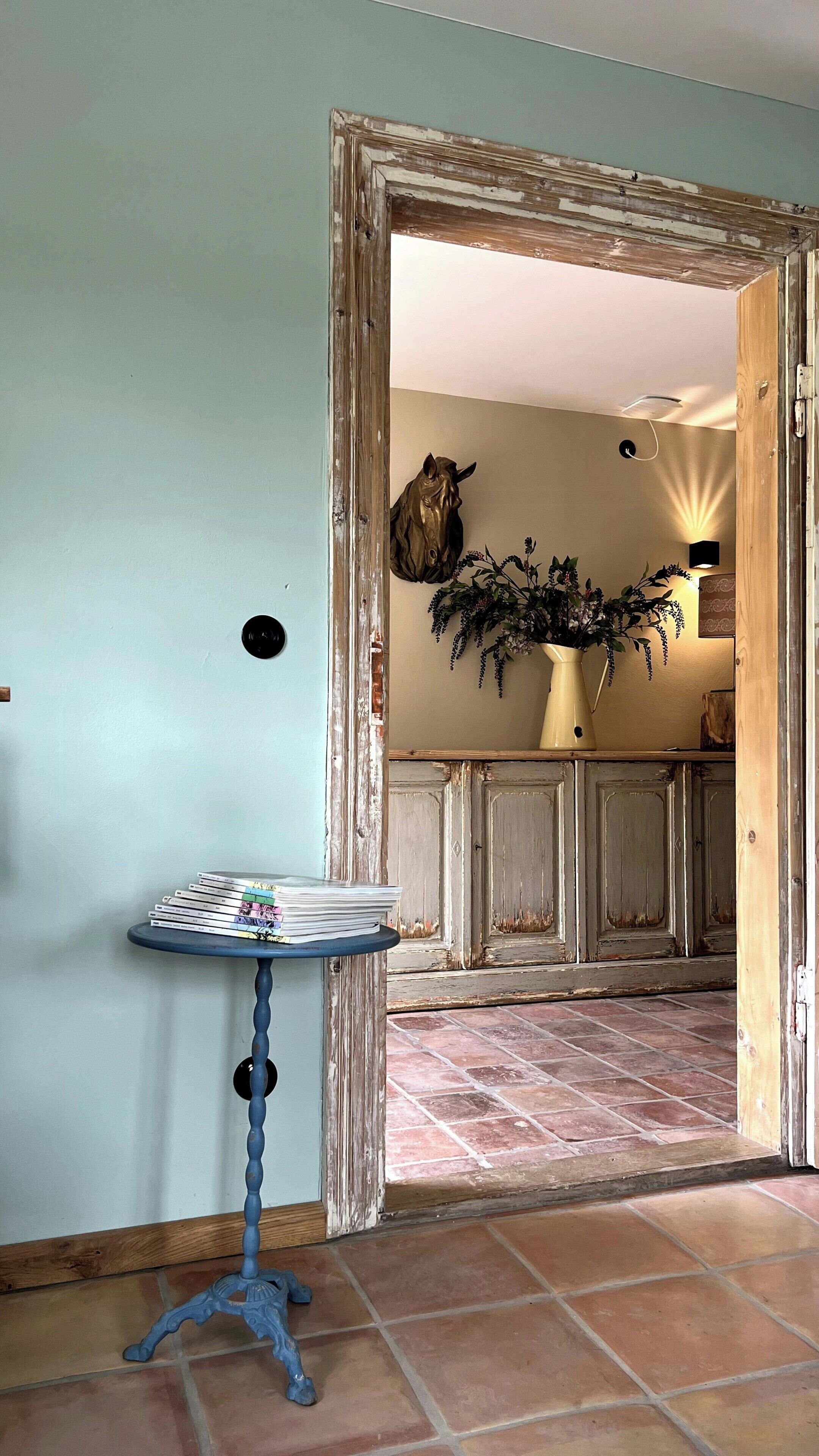Ein Zimmer mit einem rustikalen Türrahmen, einem kleinen Tisch mit einer Vase und einem an der Wand befestigten dekorativen Pferdekopf.