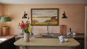 A kitchen with a sink, a vase with flowers, a painting on the wall, and two wall-mounted lamps.