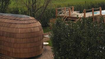 Eine Holzterrasse mit Liegestühlen mit Blick auf einen Pool, umgeben von Grünflächen und einer Bergsicht.