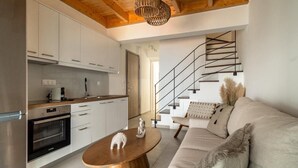 Una cuina moderna amb armaris blancs, una taula de dinar de fusta i una escala que condueix a una zona d'estar amb un sofà i coixins decoratius.