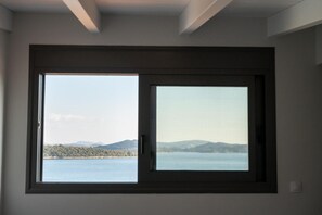 Quarto com uma grande janela com vista para um corpo de água e colinas ao longe.