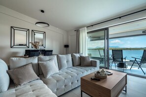 Een moderne woonkamer met een bank, een salontafel en uitzicht op de zee door grote ramen.