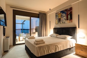 Een moderne hotelkamer met een groot bed, uitzicht op de zee, een schilderij aan de muur en een aan de muur bevestigde televisie.