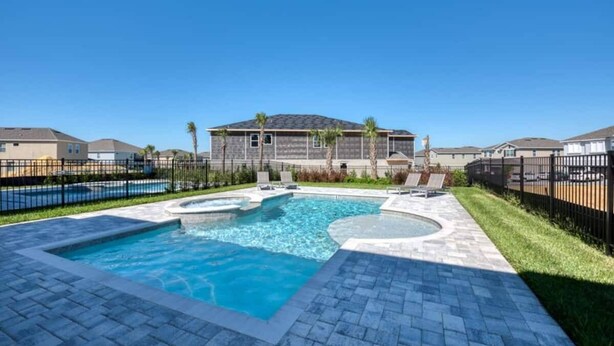 A swimming pool with a tiled deck, surrounded by a fence, and a building in the background. - Elegant Disney Retreat! Private Pool, Spa & Game Room - Sleeps 12 (Kissimmee)