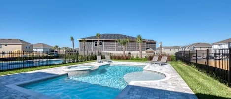 A swimming pool with a tiled deck, surrounded by a fence, and a building in the background.