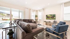 A modern living room with a sofa, a glass coffee table, and a TV. - Elegant Disney Retreat! Private Pool, Spa & Game Room - Sleeps 12 (Kissimmee)