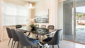 A modern dining room with a glass table, dark chairs, a chandelier, and a large abstract painting. - Elegant Disney Retreat! Private Pool, Spa & Game Room - Sleeps 12 (Kissimmee)