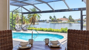 Un espace piscine avec vue sur un plan d’eau, des chaises longues et une table avec une tasse et une soucoupe.