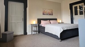 A bedroom with a bed, bedside tables, a wall-mounted artwork, and a door. - Kuhstall Apartment with Shared Terrace, Garden and Wi-Fi (Wurster Nordseeküste)