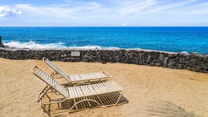A beach with two sun loungers and a stone wall. - Casa Emdeko A117 2 Bedroom Condo (Kailua-Kona)