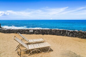 A beach with two sun loungers and a stone wall. - Casa Emdeko A117 2 Bedroom Condo (Kailua-Kona)