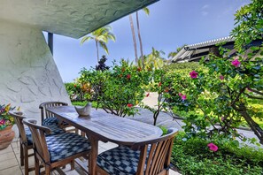 An outdoor seating area with a table and chairs, surrounded by lush greenery and flowering plants. - Casa Emdeko A117 2 Bedroom Condo (Kailua-Kona)