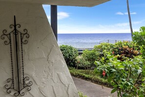 A view of the ocean from a balcony with a railing, surrounded by greenery and a decorative metal piece. - Casa Emdeko A117 2 Bedroom Condo (Kailua-Kona)