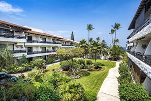 A hotel courtyard with multiple balconies, palm trees, and a well-maintained garden. - Casa Emdeko A117 2 Bedroom Condo (Kailua-Kona)