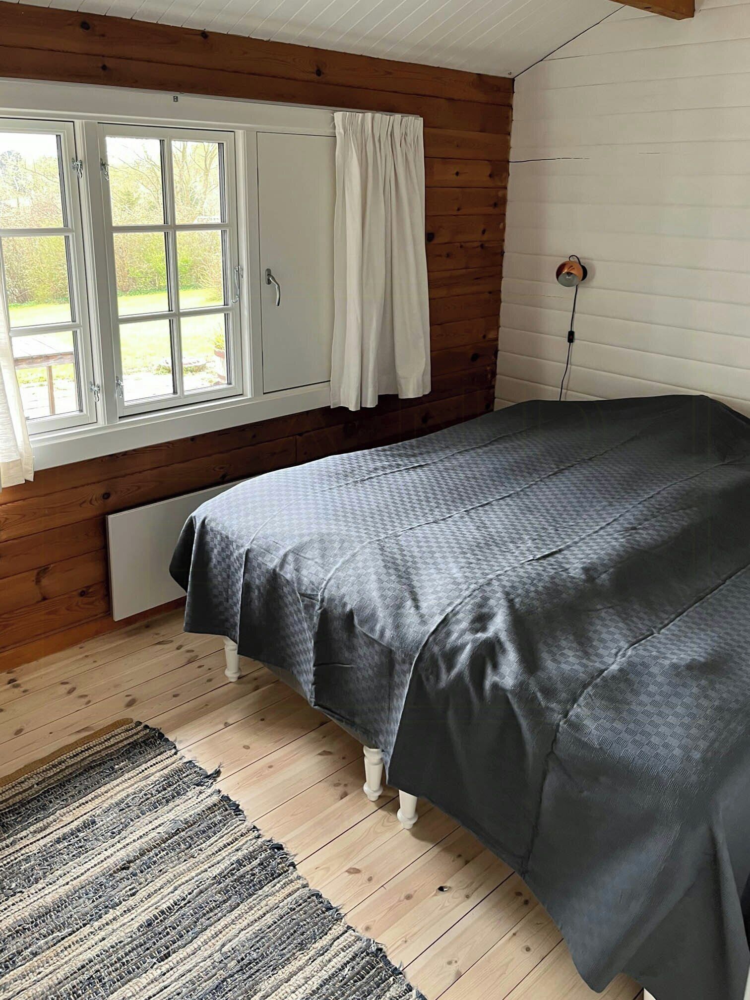 A room with a bed, wooden walls, a window with curtains, and a power outlet.