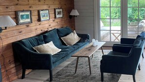 Ein gemütliches Wohnzimmer mit Holzwand, einer Couch, einem Couchtisch und Blick durch große Fenster.