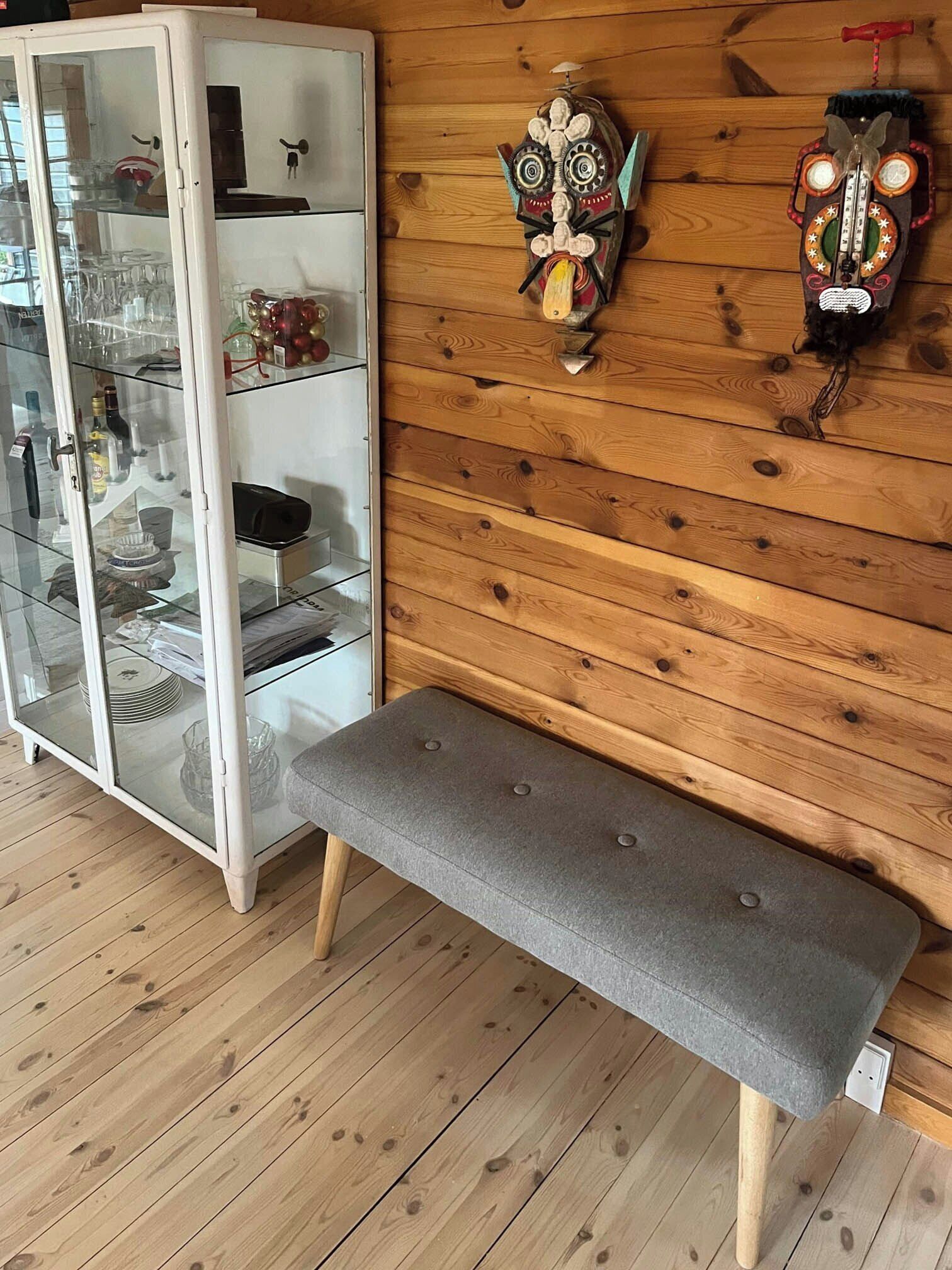Una pared de madera con dos máscaras, un aparador de vidrio y un banco gris.