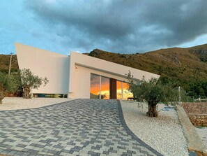 A modern building with a curved driveway, large glass doors, and a view of the sunset. - Mediterranean villa with panoramic infinity pool (Castellammare del Golfo)