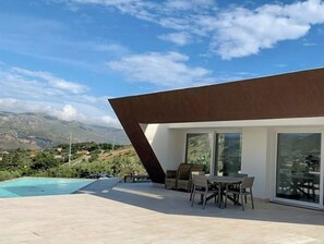 A modern outdoor patio with a pool, dining area, and a view of the mountains. - Mediterranean villa with panoramic infinity pool (Castellammare del Golfo)