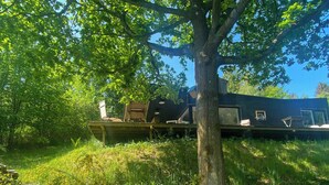 Un’imbarcazione simile a una barca, fissa a terra, con ponte, finestre e un camino, circondata da alberi e erba.