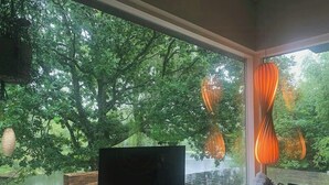 Un soggiorno moderno con una grande finestra, un televisore a schermo piatto su un supporto, un cesto di vimini e una poltrona verde.