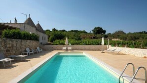 Ein rechteckiger Pool mit einer Steinsäule an einer Seite und Liegest ühlen an der anderen.