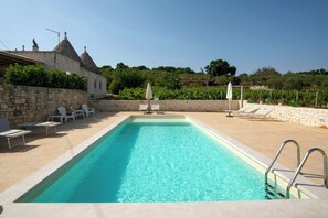 A rectangular swimming pool with a stone wall on one side and lounge chairs on the other. - 19th-century trulli complex among vineyards (Martina Franca)