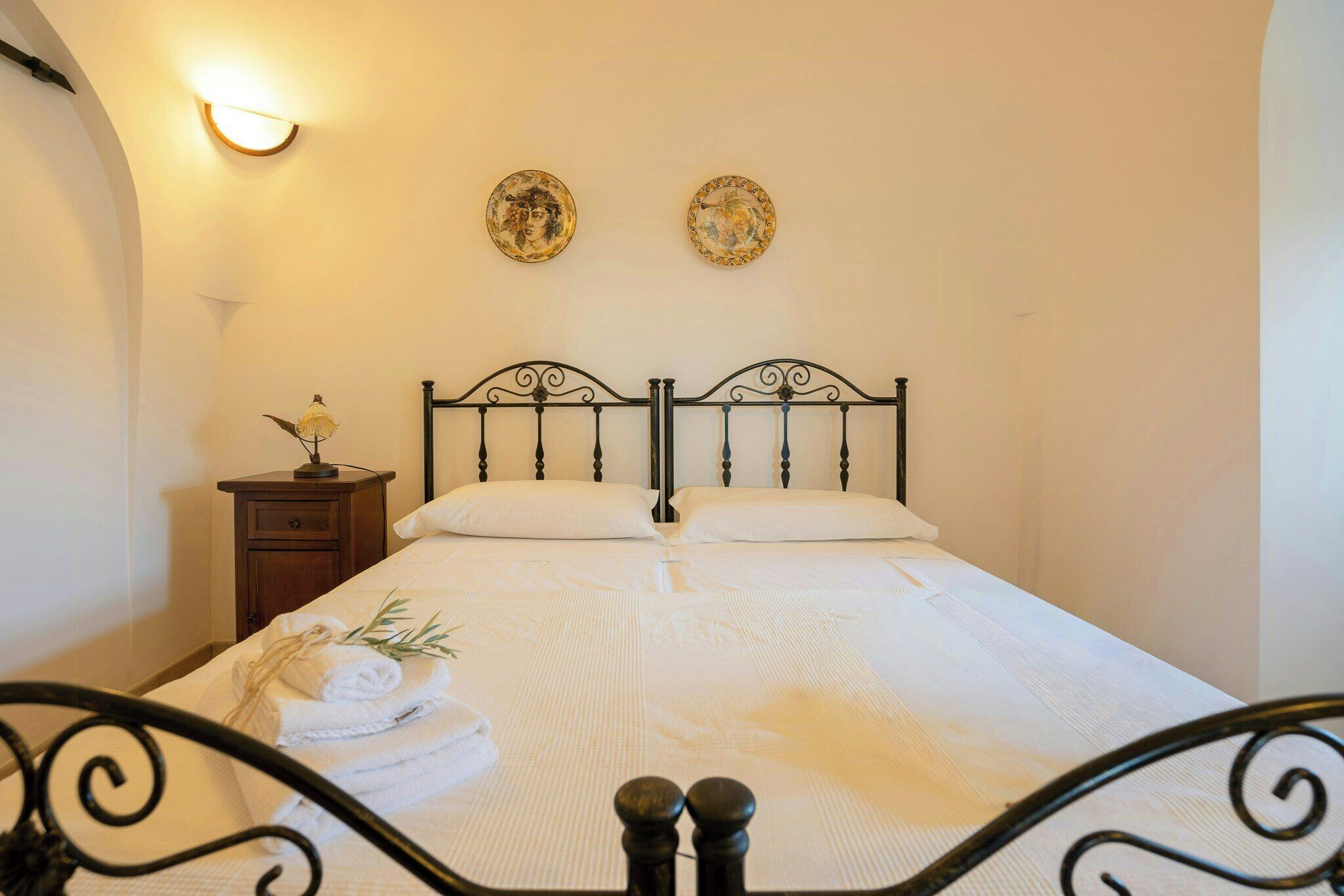 A neatly made bed with white linens, a small bedside table with a lamp, and two wall-mounted decorative plates.