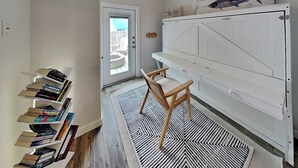 A room with a bookshelf, a wooden chair, a patterned rug, and a white cabinet. - The Flip Flop Flat | Updated, Pet Friendly, & Community Pool (Port Aransas)