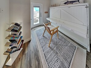 A room with a bookshelf, a wooden chair, a patterned rug, and a white cabinet. - The Flip Flop Flat | Updated, Pet Friendly, & Community Pool (Port Aransas)