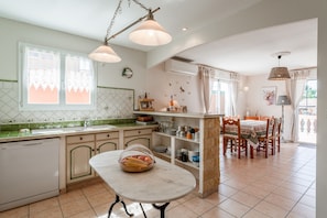 Une cuisine avec coin repas, comprenant une table en marbre, des meubles en bois et un luminaire suspendu.