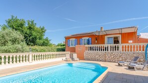 Una piscina amb un mur de pedra i un edifici amb persianes blaves.