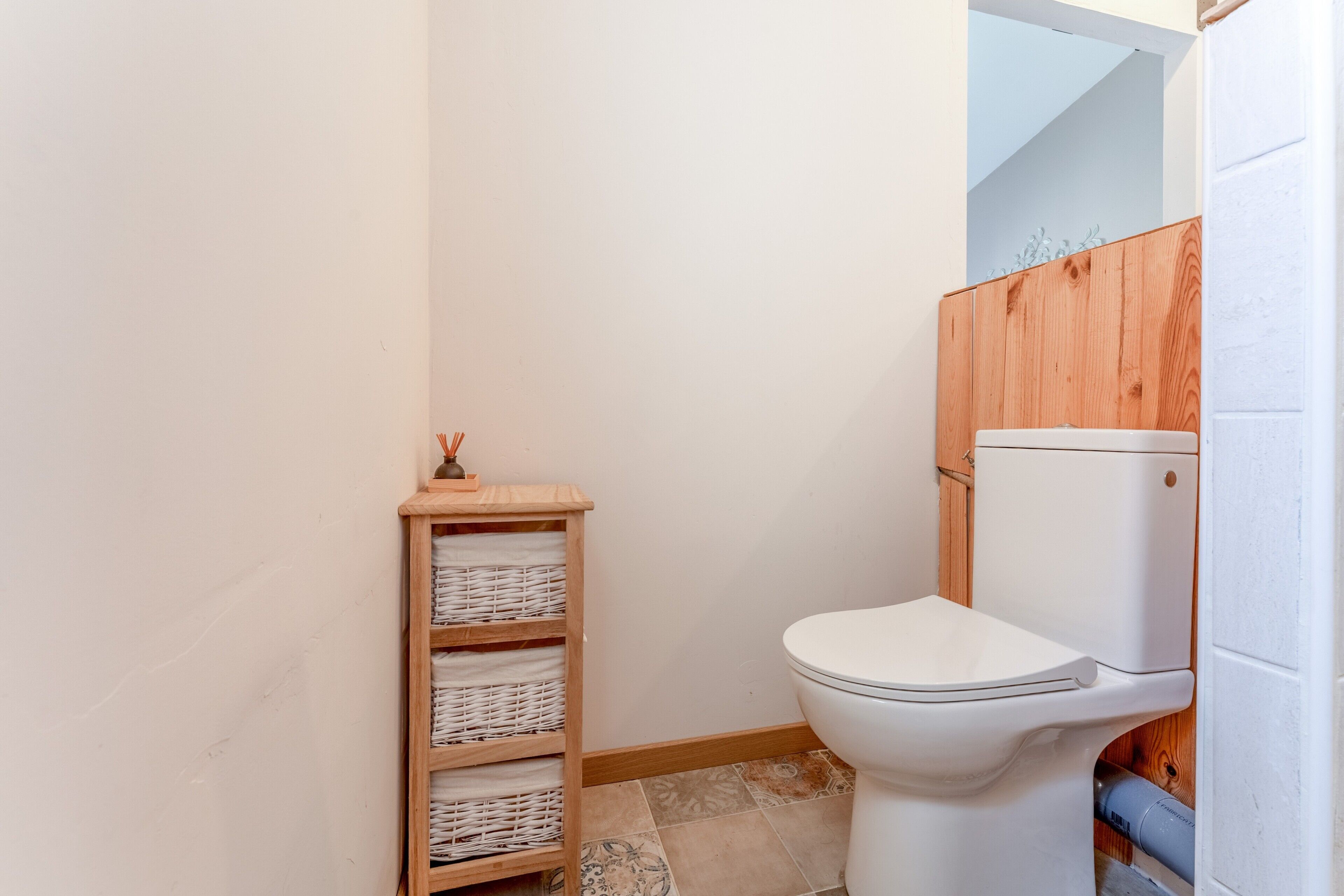 Een kleine badkamer met een wit toilet, een houten plank met manden en een houten wandpaneel.
