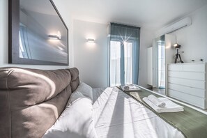Une chambre d’hôtel moderne équipée d’un lit, d’une table de chevet, d’un miroir, d’une commode et d’une fenêtre avec des rideaux.
