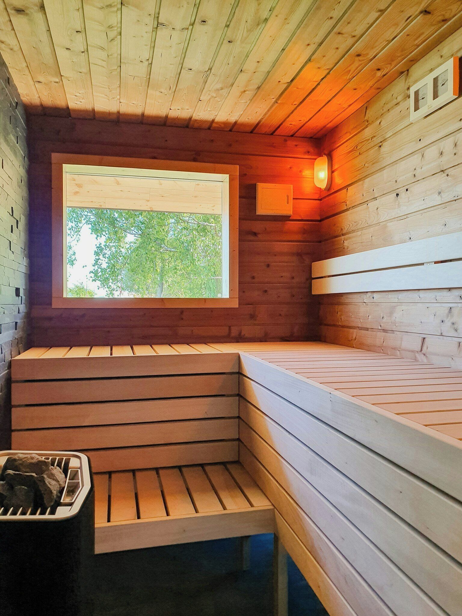 A sauna with wooden benches, a window, and a wall-mounted light fixture.