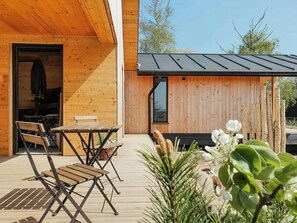 A wooden deck with a table and chairs, a wooden structure with a window, and a garden area with plants. - Luxury chalet with sea view at Salzhaff (Boiensdorf)