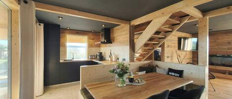 Een moderne keuken met houten balken, een eethoek met een houten tafel en zwarte stoelen, en een trap.
