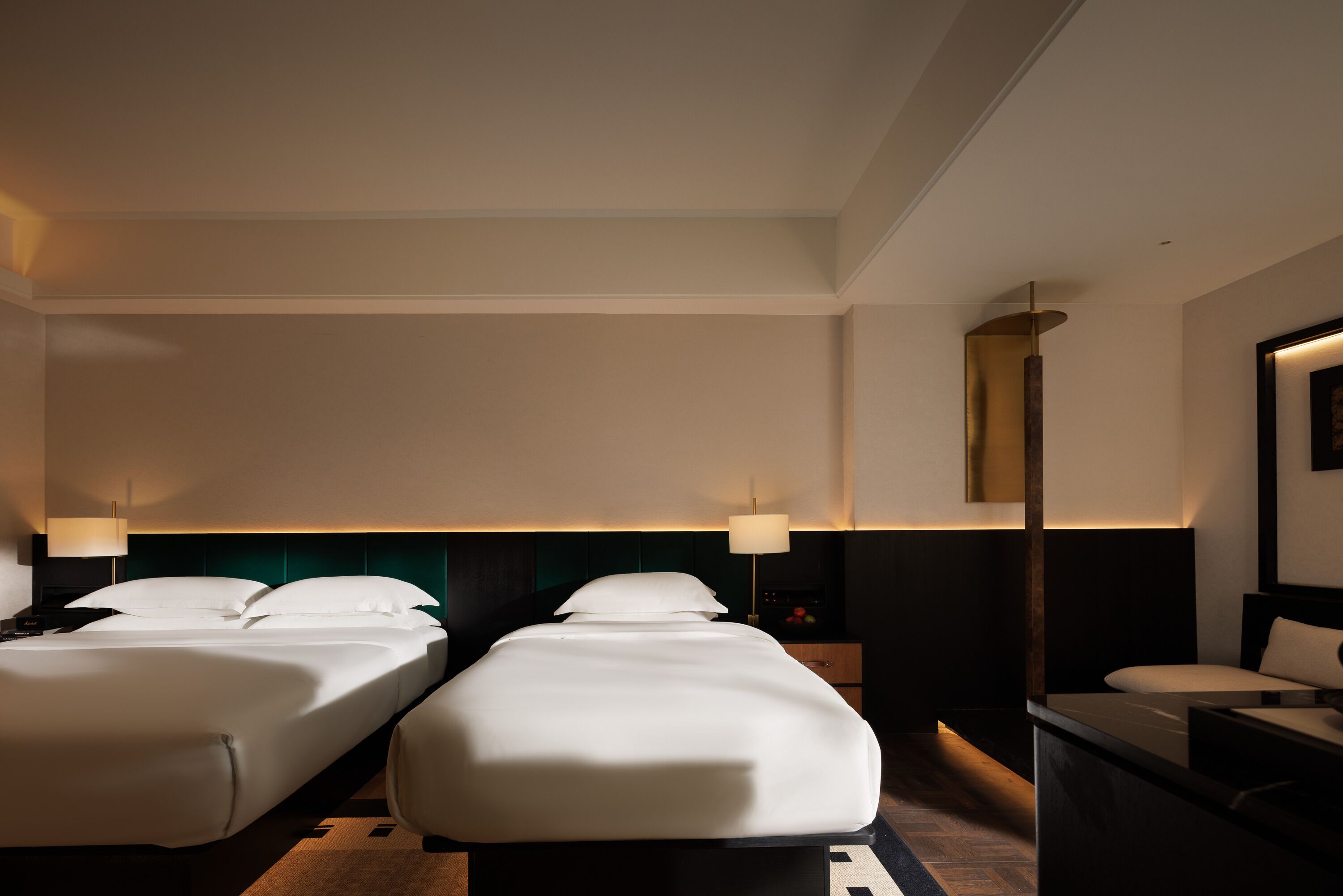 Une chambre d’hôtel avec deux lits, un bureau, une chaise, une table de chevet et une lampe.