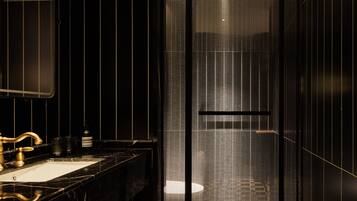 Un baño moderno con piso a cuadros blancos y negros, ducha con cerramiento de vidrio y tocador con grifo dorado.