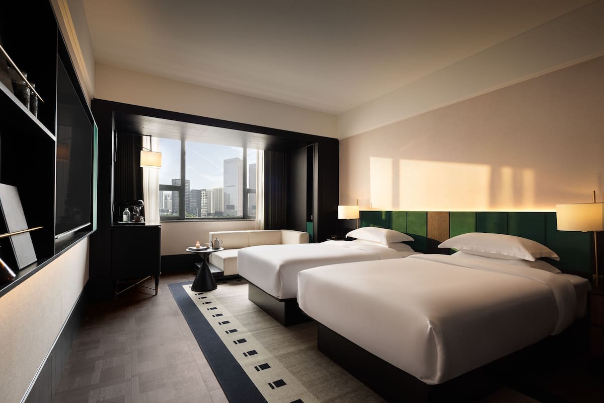 Habitación de hotel con dos camas, un sofá, un televisor, un escritorio y vistas a la ciudad.