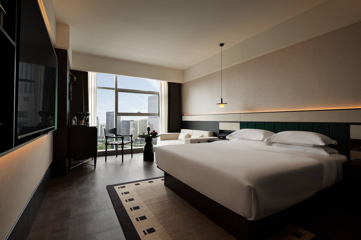 Una habitación de hotel con una cama grande, un escritorio, una silla, un televisor y una ventana con vistas a la ciudad.