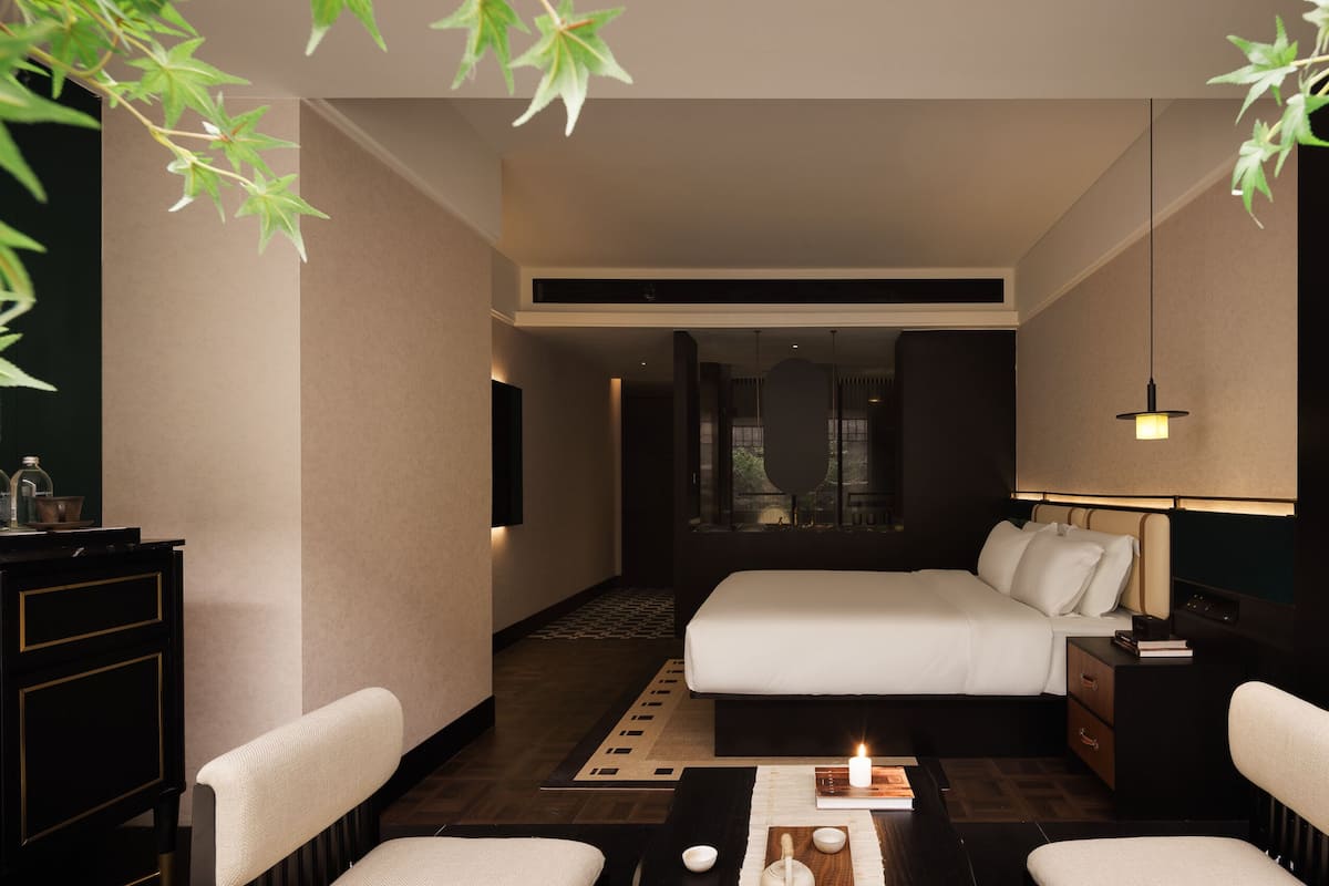 Habitación de hotel con cama, mesitas de noche, escritorio, sillas, espejo y vistas al exterior.