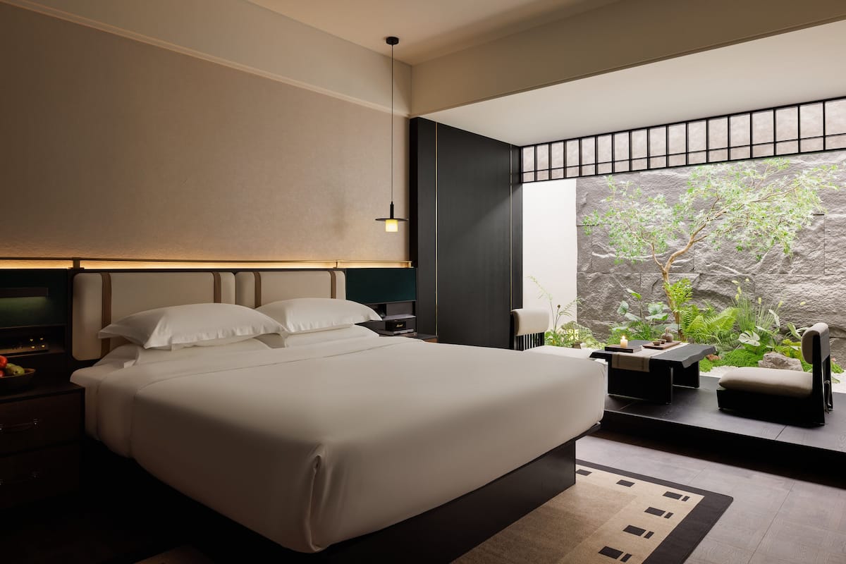Un dormitorio moderno con una cama grande, mesitas de noche, un escritorio y vistas a la vegetación a través de una ventana.