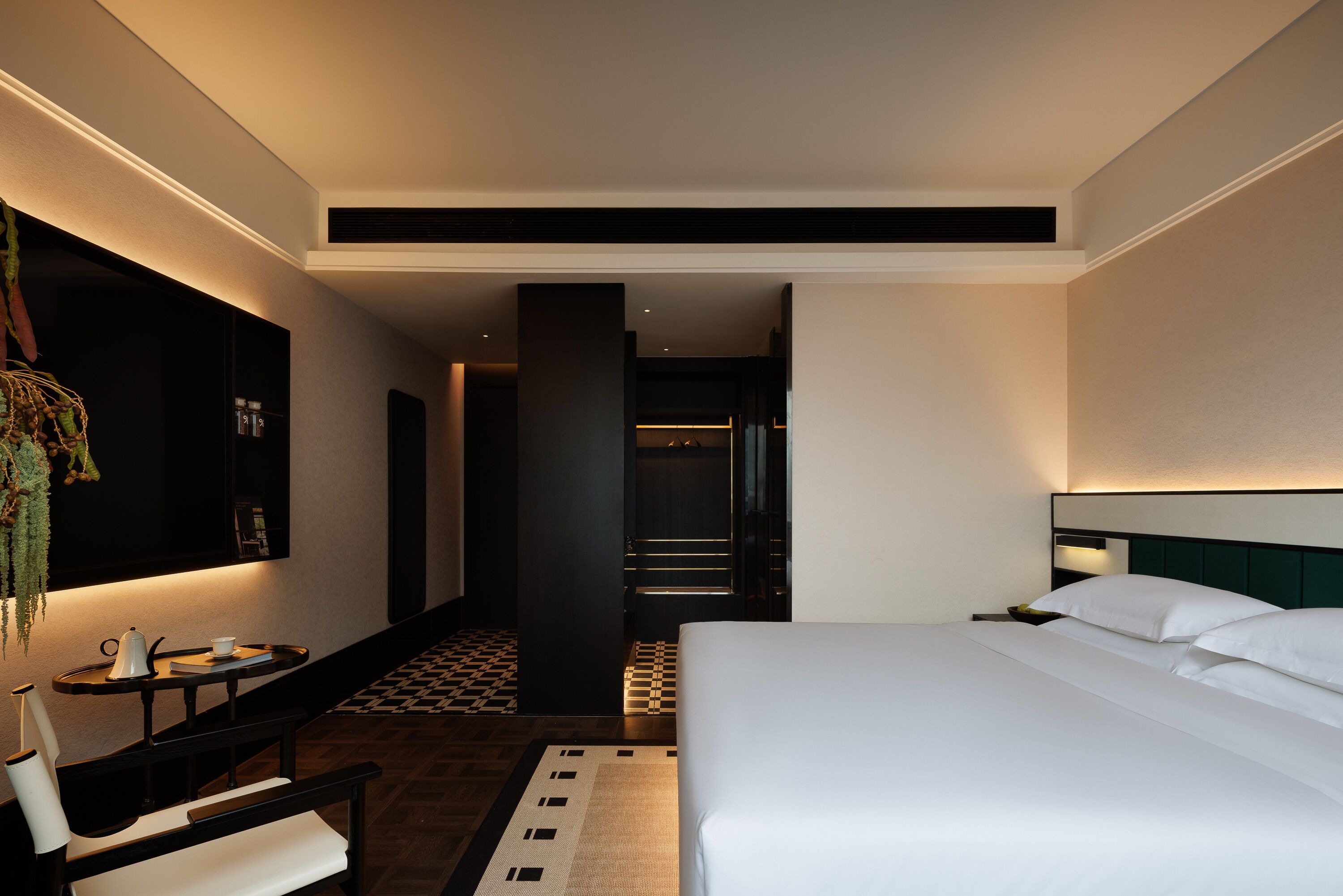A hotel room with a bed, a desk with a chair, a small table with a kettle, and a checkered floor.
