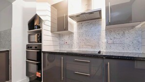 A modern kitchen with built-in appliances, marble backsplash, and sleek cabinetry. - Spacious 4BR City Centre Apartment Dundee (Dundee)