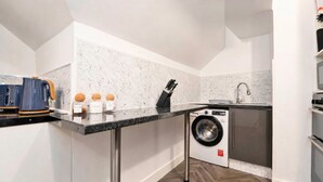 A compact kitchen with a washing machine, a coffee maker, and a knife block. - Spacious 4BR City Centre Apartment Dundee (Dundee)