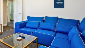 A blue sofa with a glass coffee table, a white door, and a wall with a logo. - Spacious 4BR City Centre Apartment Dundee (Dundee)