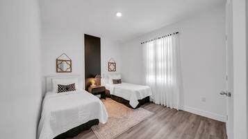 Quarto com duas camas, uma mesinha de cabeceira, um tapete e uma janela com cortinas.